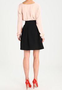 Gonna nera svasata con pieghe, abbinata a una blusa rosa chiaro e scarpe con tacco rosso. Tessuto morbido, design a strati e vita aderente.