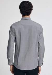 Svartvit rutmönstrad skjorta med knappar, lång ärmad och med klassisk krage. Har små kontrasterande knappar vid manschetterna.