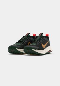 Black running shoes with green accents and a brown Nike swoosh. Features a textured upper, laces, and a red heel tab. Thick, rugged sole.