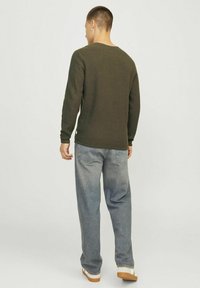Tricou cu mânecă lungă din tricot cu model waffle, de culoare verde măsliniu, cu guler tip crew neck, purtat cu blugi drepți de culoare albastru deschis și teneși albi cu talpă bej.