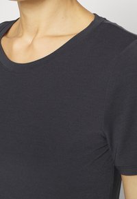 T-shirt grigio scuro a maniche corte con scollo rotondo, realizzato in tessuto morbido, con un design aderente e dettagli delle cuciture sottili ai lati.