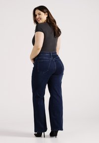 Donkerblauwe rechte jeans met een hoge taille, voorzien van achterzakken en een gladde, rekbare stof. Gecombineerd met een aansluitend grijs shirt.