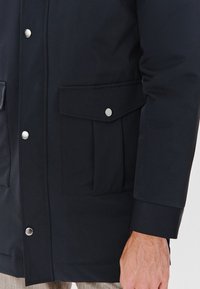 Granatowa kurtka wykonana z gładkiego, wodoodpornego materiału. Posiada zamek błyskawiczny, napy oraz dwie przednie kieszenie naszywane.