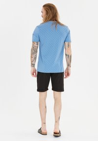 Blå kortärmad skjorta med vita prickar, kombinerad med svarta shorts. Skjortan har rund halsringning och en avslappnad passform.