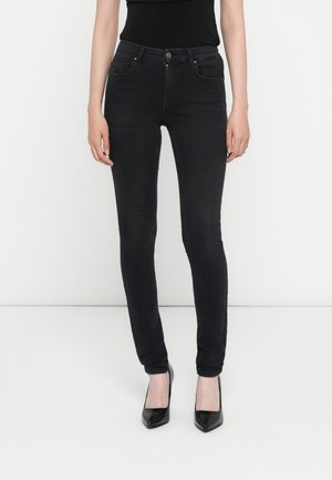 Jean skinny noir en denim, avec poches avant, fermeture à bouton et silhouette ajustée, associés à des escarpins noirs à talons pointus.