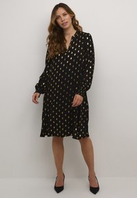 Črna obleka z zlatimi lističi, dolgi rokavi, V-izrez in nagubani manšeti. Gladek material, do kolen, v kompletu s črnimi petkami.