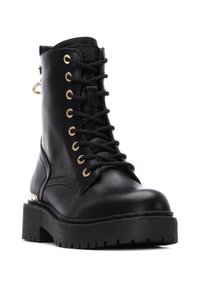 Bota negra de cuero con cordones, ojales dorados, suela gruesa negra, tacón prominente y detalle de hardware lateral. Textura suave, diseño robusto.