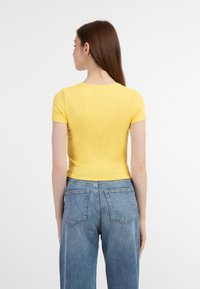 Top galben cu maneci scurte și croială ajustată, asociat cu blugi blue cu talie medie, având un design clasic cu cinci buzunare.
