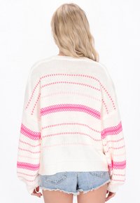 Maglione bianco lavorato a maglia con strisce orizzontali rosa, caratterizzato da maniche larghe e orlo a coste. Indossato sopra pantaloni di jeans, per un look informale.