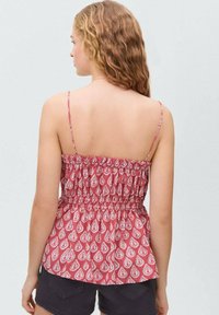 Red patterned top with thin straps and gathered detail at the waist, paired with black shorts. Intricate paisley print throughout.