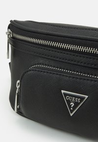 Čierny nylonový fanny pack so striebornými zipsami, prednou kapsou a trojuholníkovým logom. Má textúrovaný povrch a dvojité ťaháky na zips.