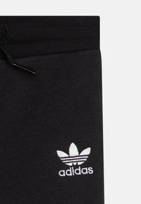 Pantaloni della tuta neri in cotone con logo trefoil Adidas ricamato in bianco e cordino in vita. Texture liscia, design casual.