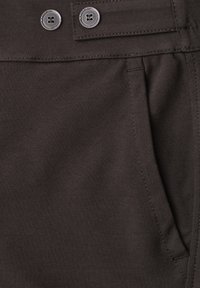 Dark fabric close-up showing a pocket with detailed stitching and two buttons on a waistband tab.