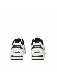 Scarpe sportive bianche e nere con tomaia perforata, collare imbottito e suola in gomma. Presentano un logo sul tallone e accenti texturizzati.