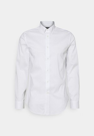 Langärmeliges weißes Hemd mit Knöpfen, feinem gepunktetem Muster und geknöpftem Kragen vor schlichtem hellem Hintergrund.