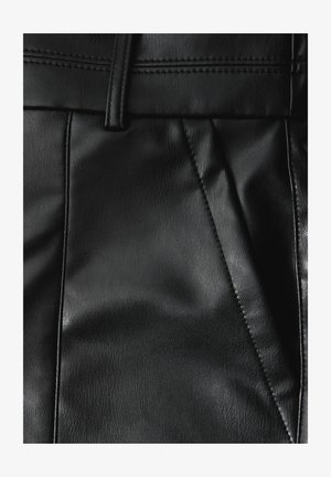 Zwarte leren broek met een soepele textuur, voorzien van voorplooien en een slim-fit ontwerp. Gestikte details langs de tailleband.