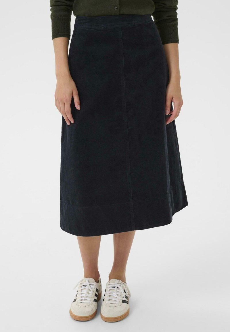 Jupe midi en velours côtelé marine avec une coupe droite et une texture subtile, associée à des baskets blanches avec des rayures noires.