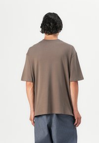 Brown cotton t-shirt with short sleeves, crew neck, and relaxed fit, paired with blue denim pants. Minimalist design, no visible patterns or logos.