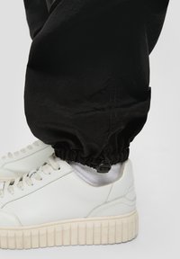Witte leren sneakers met gestructureerde zolen, gecombineerd met zwarte elastische broek met cuffs en een koorddetail aan de onderkant.