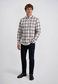 Heren overhemd met lange mouwen in een geruit patroon met wit, bordeauxrood en groen, knoopsluiting en ronde onderkant, gecombineerd met donkere jeans en bruine schoenen.