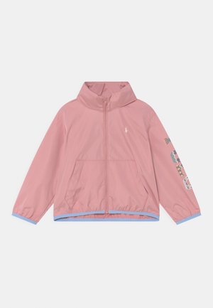 Chaqueta rosa con cremallera y cuello alto, bolsillos delanteros, ribete azul claro y texto "POLO" con diseño floral en la manga derecha.