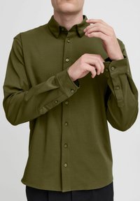 Olive green long-sleeve shirt with a button-down collar, featuring a front placket with buttons, adjustable cuffs, and a smooth texture.