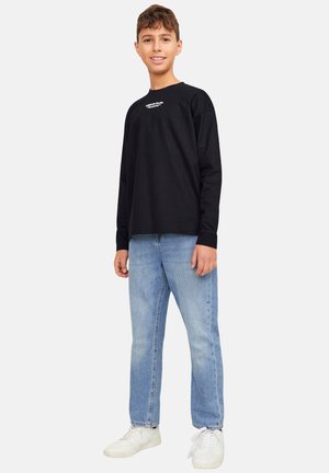 Sort langærmet skjorte med hvid tekst, parret med lyseblå jeans og hvide sneakers. Snittet er afslappet med en løs silhuet.