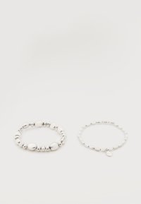 Deux bracelets de perles argentées sur fond blanc ; l'un avec des perles irrégulières et l'autre avec des perles uniformes et un petit charme en forme de goutte.
