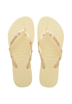 Yellow flip-flops with transparent straps, embellished with clear and pink decorative accents, cross over a textured sole.