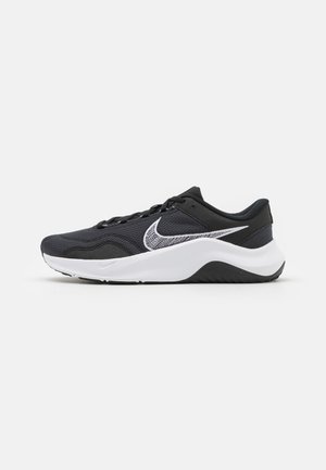 Zapatilla de correr Nike en blanco y negro con parte superior de malla, logo Swoosh blanco, diseño con cordones y suela blanca gruesa con patrón de tracción negro.