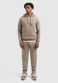 Beige hoodie met trekkoorden en logo, gecombineerd met bijpassende tapering sweatpants en neutraalgekleurde sneakers met textuuraccenten.