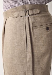 Beige test szabású nadrág lapos elülső résszel, övcsattal, oldalsó zsebbel és texturált anyaggal.