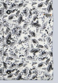 Weißer Stoff mit einem schwarz-grauen Blumenmuster, versehen mit dunklen Knöpfen und einem kleinen Markenetikett. Strukturierte Oberfläche mit geripptem Design.