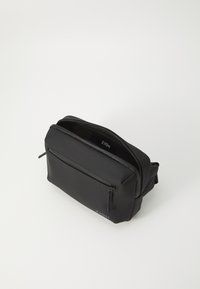 Trousse de maquillage zippée noire en matériau lisse. Comprend une poche avant, une ouverture à double zip et un logo discret à l'intérieur. Design compact.