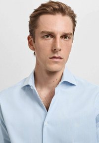 Camicia a righe blu chiaro con colletto button-down, caratterizzata da righe verticali bianche, tessuto liscio e design aderente.