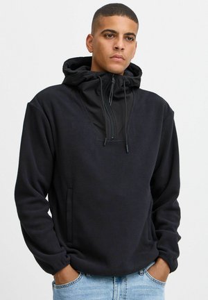 Pull en polaire noire avec capuche, doté d'une fermeture éclair mi-hauteur à l'avant, d'une poche kangourou, de poignets élastiques et d'un tissu texturé. Design simple et fonctionnel.