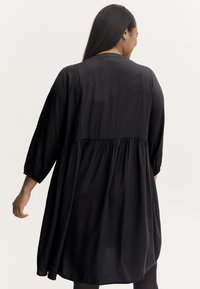 Schwarzes Kleid mit einem fließenden, gerafften Design, drei Viertelärmeln und einer glatten Textur. Es verfügt über einen runden Ausschnitt und einen lockeren Schnitt.