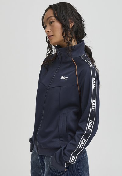 Granatowa kurtka sportowa na zamek błyskawiczny z pomarańczowymi akcentami i białymi bocznymi paskami z napisem "BALL". Wykonana z gładkiego, lekkiego materiału.