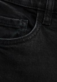 Gros plan sur un tissu en denim noir montrant les coutures et une petite poche avant avec un passant de ceinture au-dessus.
