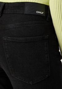Vaqueros de mezclilla negra con un diseño ajustado, que cuentan con un bolsillo trasero y una etiqueta de cuero negra con la marca grabada "ONLY" en la cintura.
