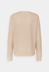 Beżowa dzianinowa bluza z teksturowanym wzorem przypominającym gofry, z okrągłym dekoltem i długimi rękawami. Szczegóły podkreślają ściągacze na mankietach i u dołu.