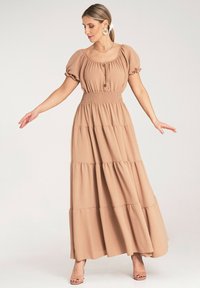 Maxi sukienka z jasnobeżowego materiału, z krótkimi bufkami, marszczonym pasem, detalami w postaci guzików oraz warstwowym krojem, zapewniającym swobodny sylwetkę.