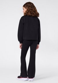 Zwarte sweatshirt en bijpassende flared broek van zacht materiaal. De outfit heeft een relaxte pasvorm, een ronde zoom en contrasterende schoenen.