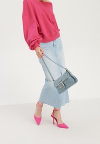 Felpa rosa off-the-shoulder, gonna di denim azzurro chiaro, décolleté rosa con tacco e una piccola borsa grigia con dettaglio a fibbia.