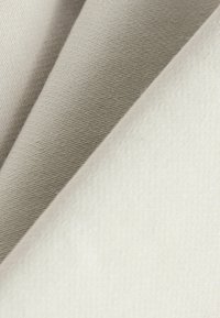 Teksturirana tkanina u nijansama off-white i svijetlosive, koja prikazuje glatku površinu s suptilnim nabiranjem i presavijenim slojevima za dubinu.