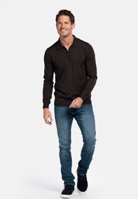 Dunkelbrauner Pullover mit Viertelreißverschluss, langen Ärmeln und weicher Textur, kombiniert mit blauen Jeans und schwarzen Schuhen.