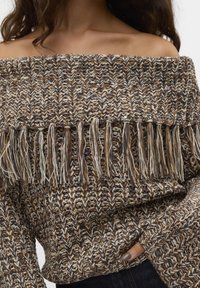 Sweter na jedno ramię z dzianiny w ziemistych odcieniach, z teksturowanym wzorem i frędzlami na dole. Miękki materiał o luźnym kroju.