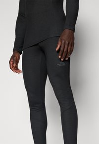 Top nero a maniche lunghe e leggings aderenti in tessuto elasticizzato, con una sottile texture e un logo sulla gamba.