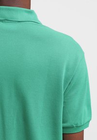 Grön polo t-shirt med en strukturerad, andningsbar tyg, klassisk krage och korta ärmar, som visar en ren och enkel design.