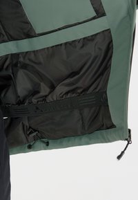 Grön och svart mellanlagerjacka med en slät yttermaterial, quiltad inredning, justerbar dragsko i nederkant och märkes-elastiskt band.